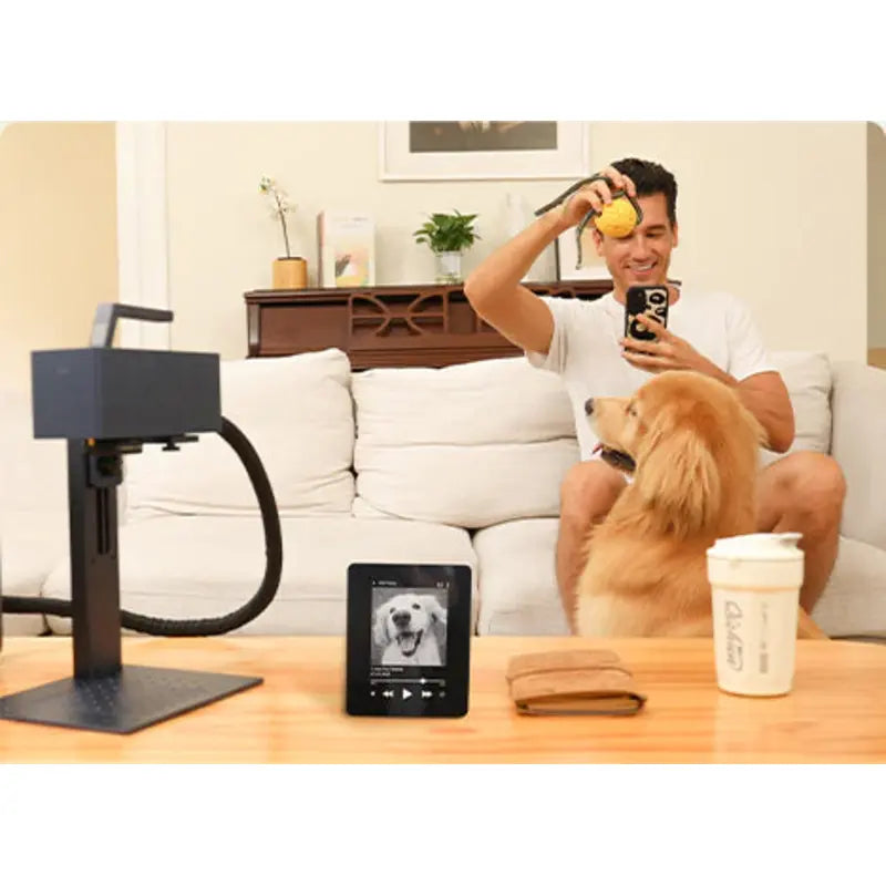 a man sitting on a couch with his dog infront of him while holding a tennis ball with the g2 laser etc. on the table towards his right