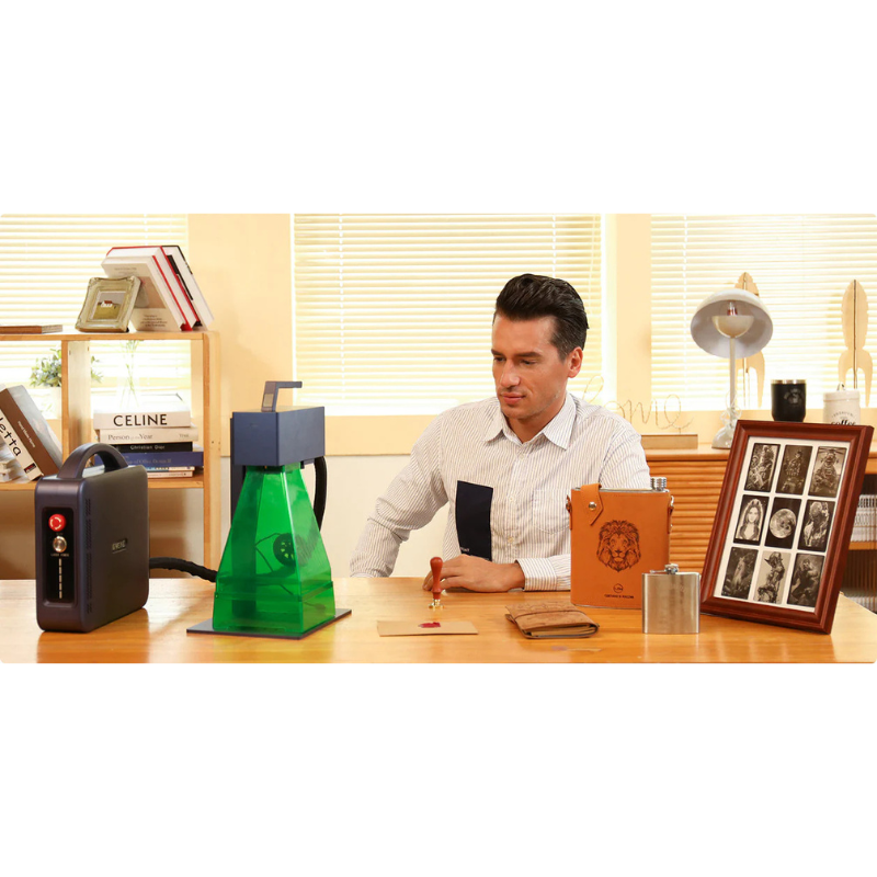 a man in a workspace seated in front of a g2 max fibre laser engraver with various engraved materials