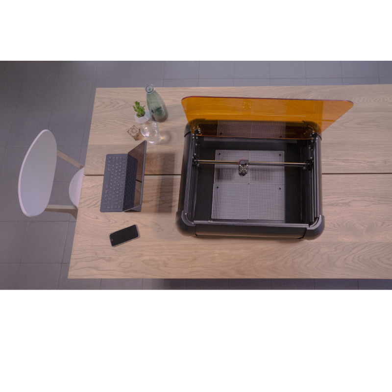 high angle view of emblaser 2 10 watt laser cutter and engraver with an open lid on a wooden desk